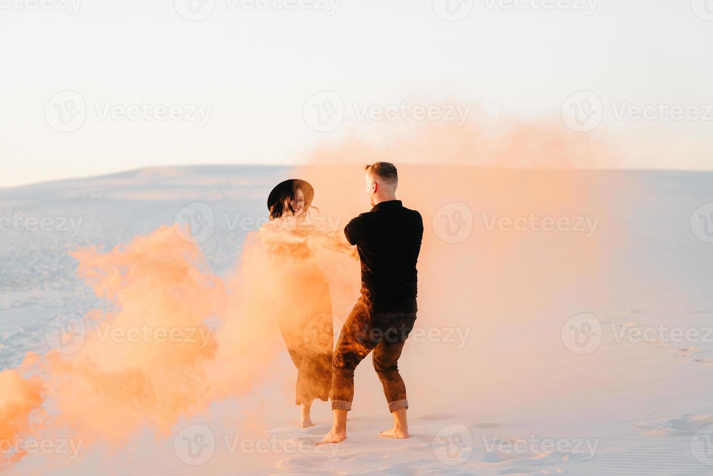 mec et une fille en vêtements noirs étreignent et courent sur le sable blanc avec de la fumée orange photo
