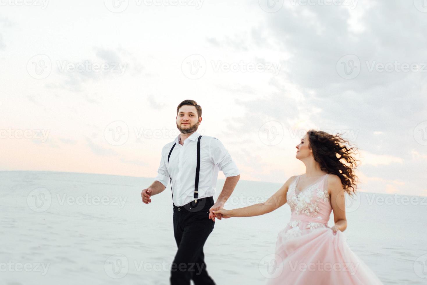 jeune couple un mec en culotte noire et une fille en robe rose marchent le long du sable blanc photo