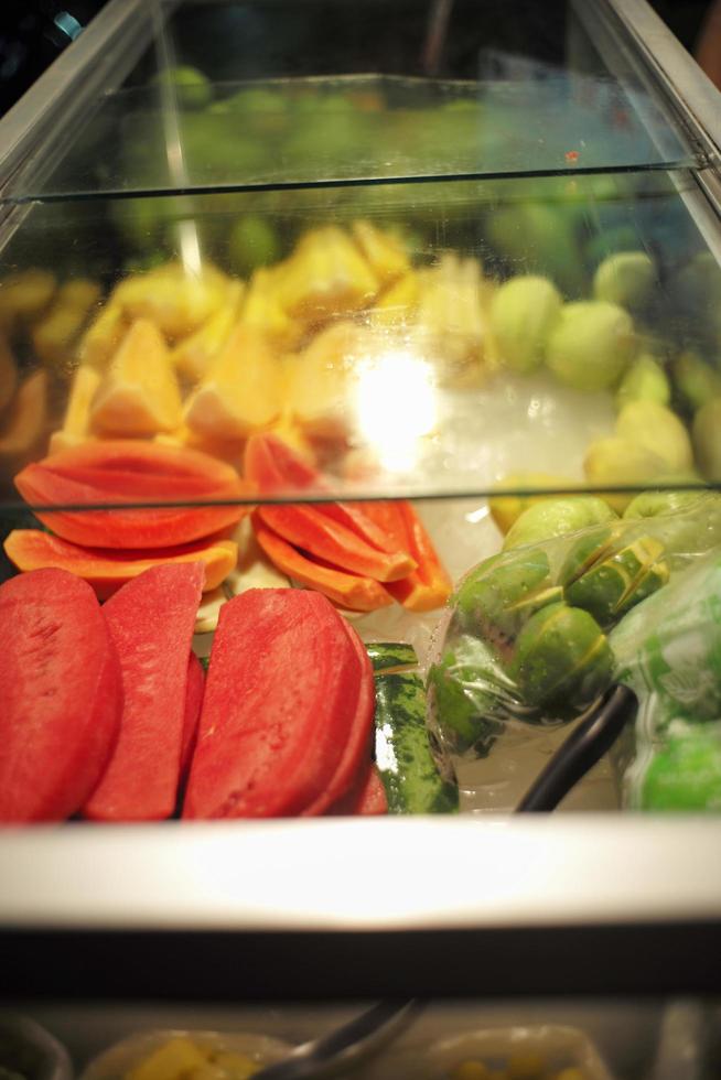 Divers fruits dans une glacière en verre à un étal de nourriture de rue dans un marché de nuit. photo