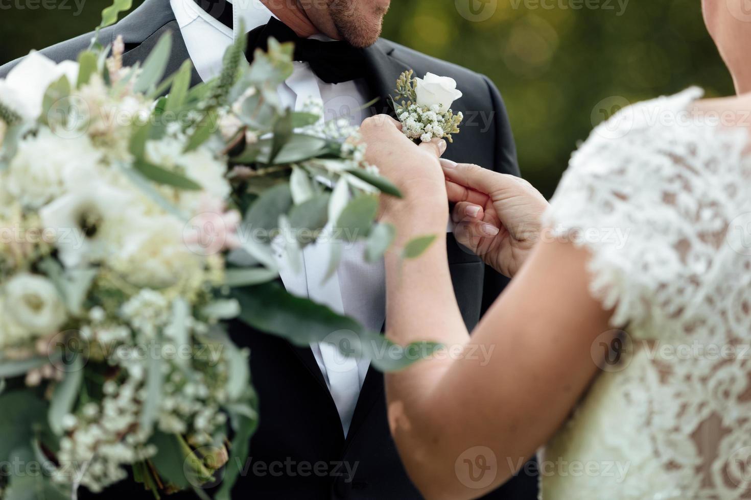 la mariée porte une boutonnière avec des roses blanches pour le marié photo