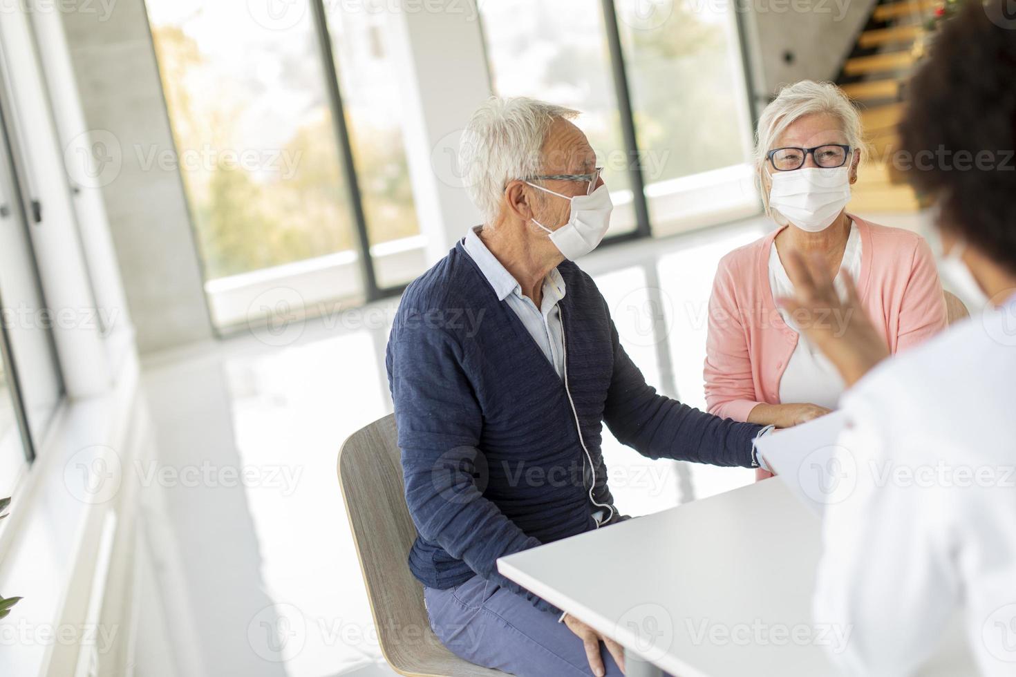 couple d'âge mûr au bureau du médecin portant des masques photo