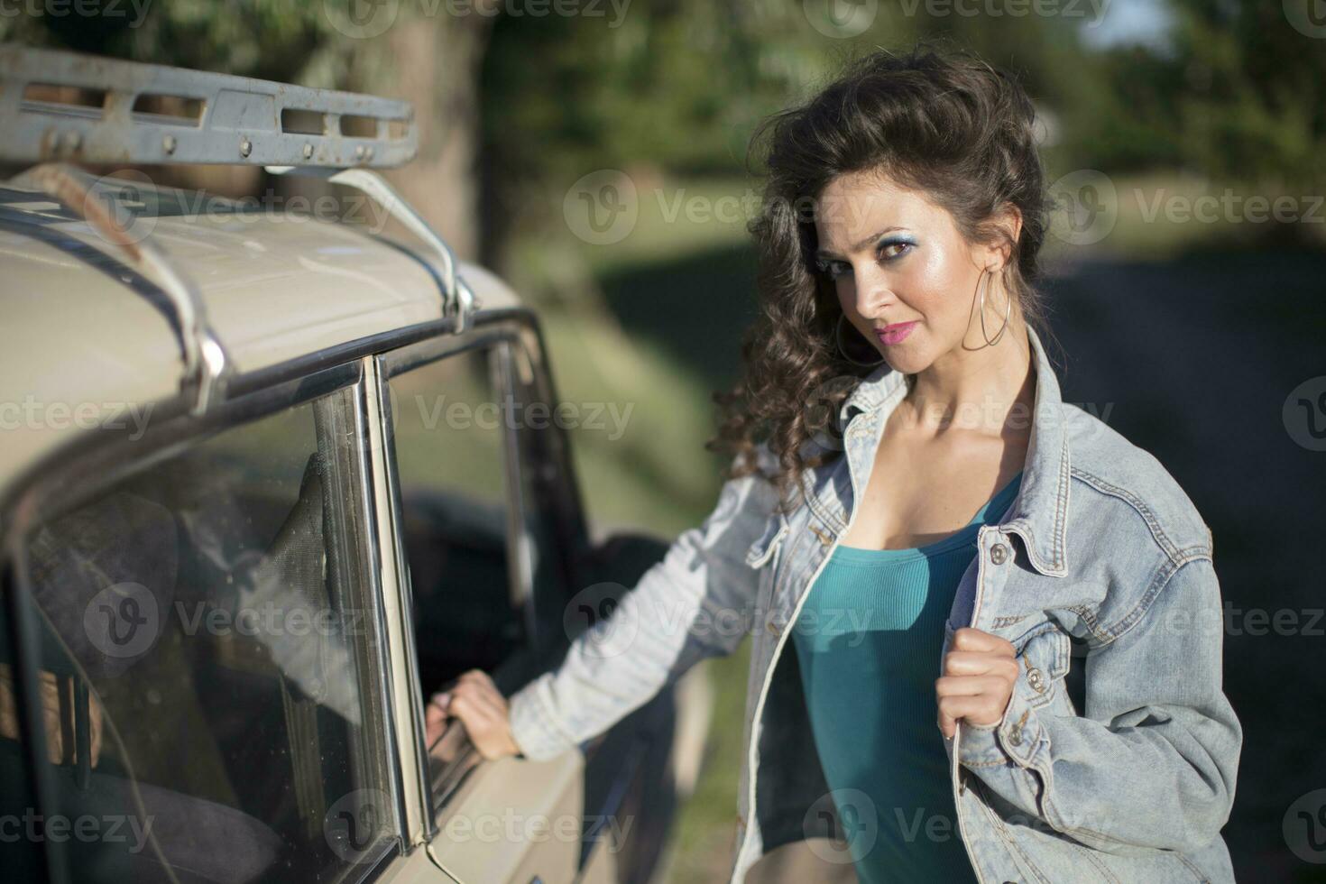 marrant Jeune femme dans une denim veste avec brillant maquillage sur le Contexte de un vieux auto. photo