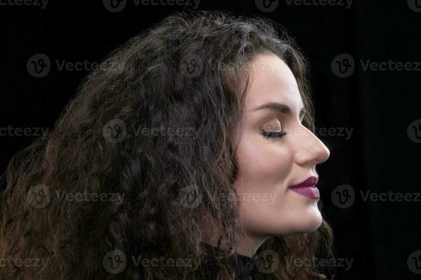 le visage de une brunette fille avec frisé cheveux dans profil sur une foncé Contexte. photo