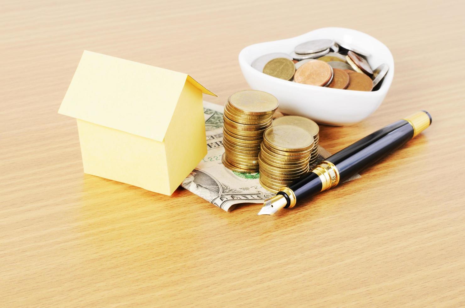 Papier maison et stylo plume avec pile de pièces d'argent sur fond de bureau en bois photo