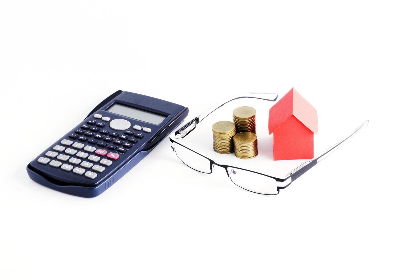 Calculatrice et lunettes avec pile de pièces et papier maison sur fond blanc photo