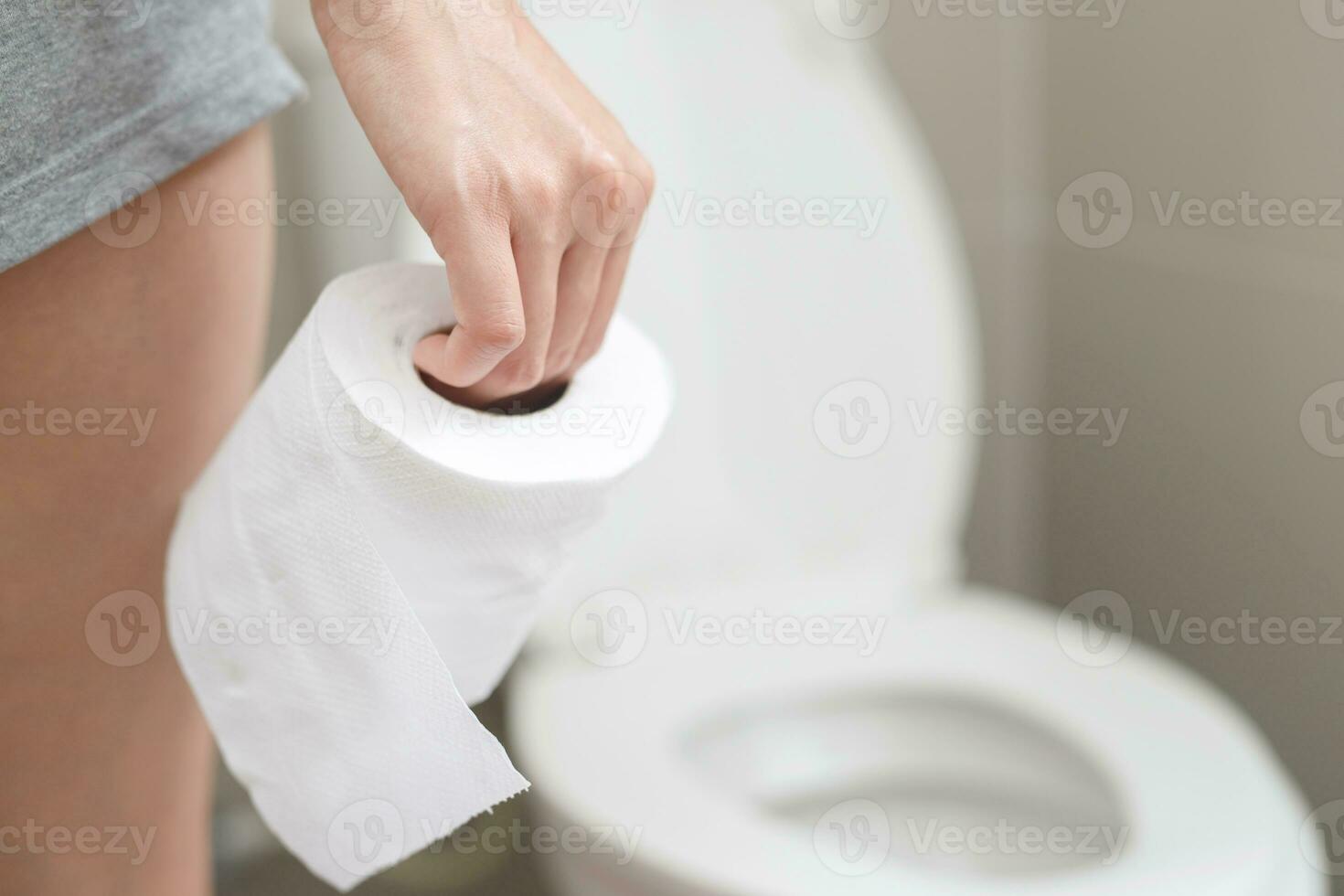 portrait de une femme souffre de la diarrhée le sien estomac douloureux. mal et problème. main tenir tissu papier rouleau dans de face de toilette bol. constipation dans salle de bains. hygiène, santé se soucier concept. photo