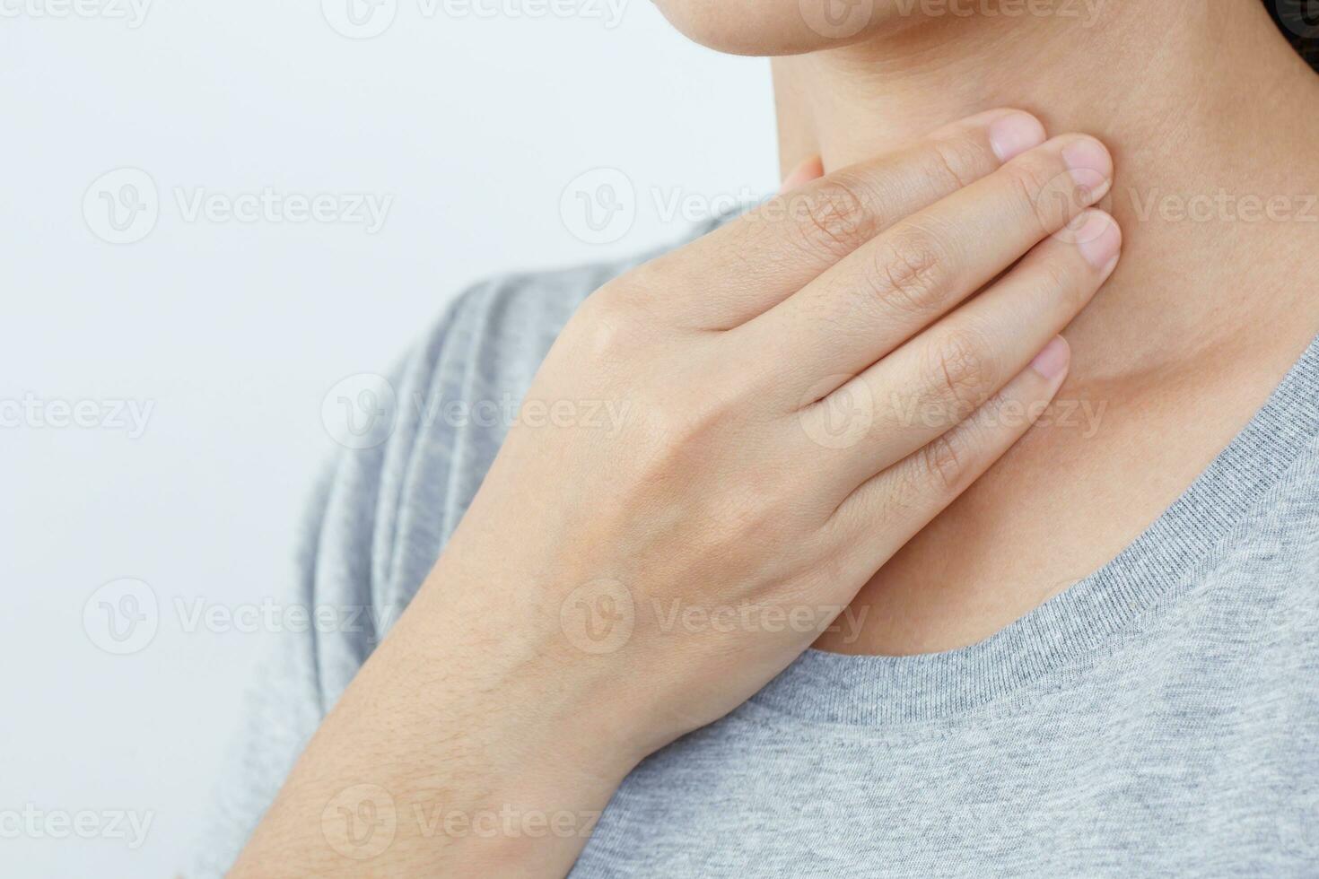 endolori gorge douleur. fermer de Jeune femme malade en portant sa enflammé gorge en utilisant mains à toucher le mauvais cou dans bleu chemise sur gris Contexte. médical et soins de santé concept. concentrer rouge sur à spectacle douleur photo