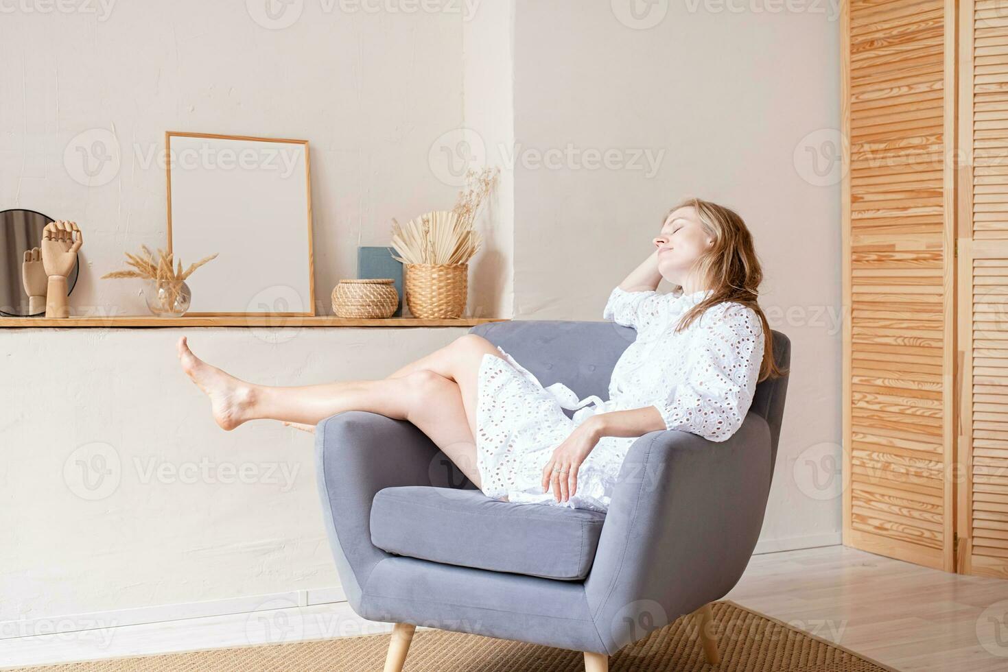 magnifique femme dans mode robe séance sur doux chaise pieds nus sur blanc mur Contexte photo