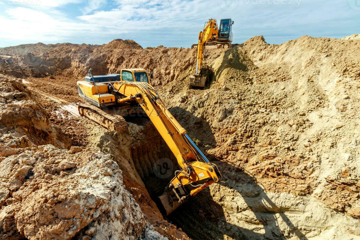 deux excavatrice sont creusement sol dans le construction site sur ciel arrière-plan, avec blanc duveteux nuage photo