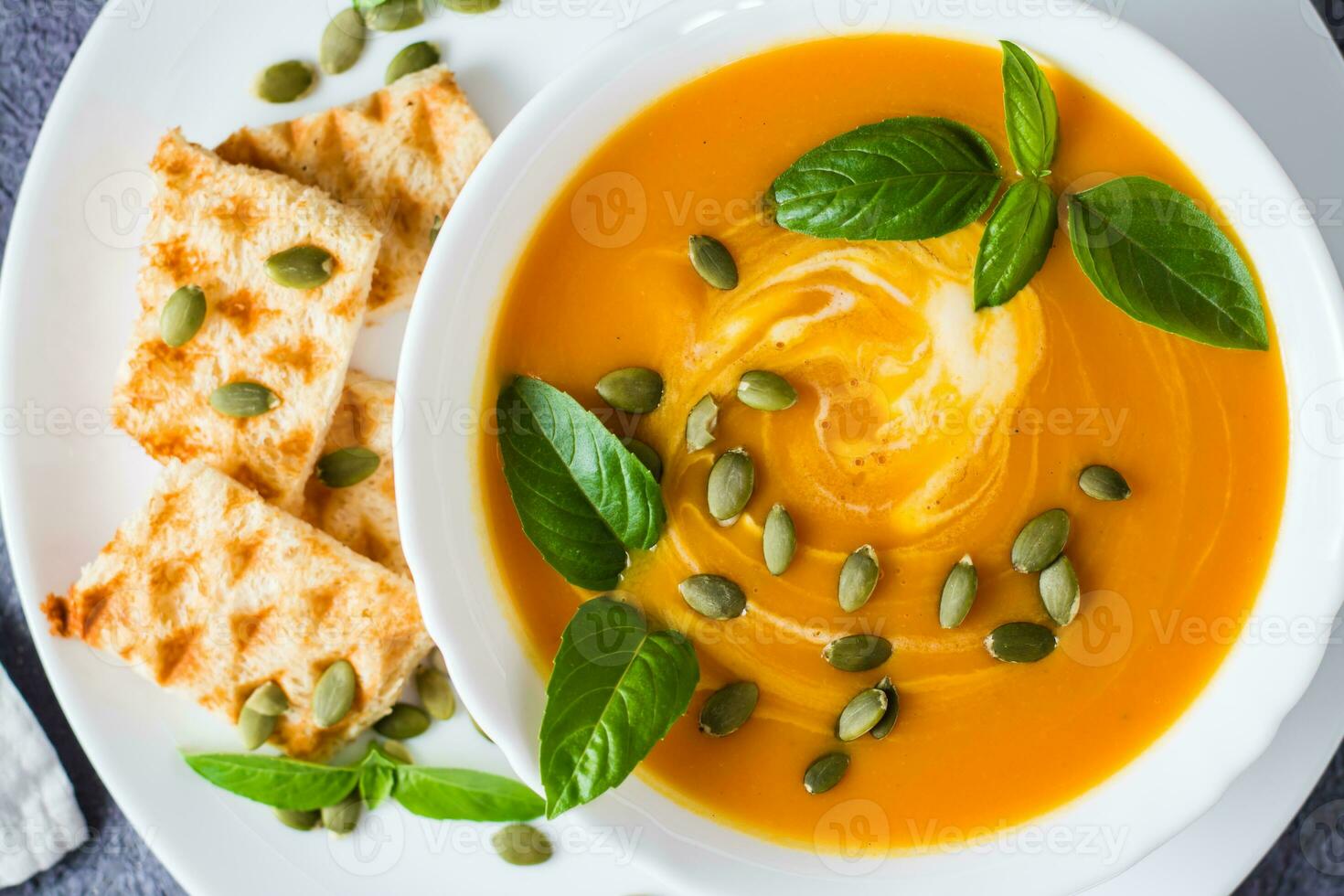 prêt à manger citrouille purée soupe avec citrouille graines, basilic feuilles et pain grillé dans une assiette sur le tableau. végétarien aliments. action de grâces journée. Haut voir. fermer photo