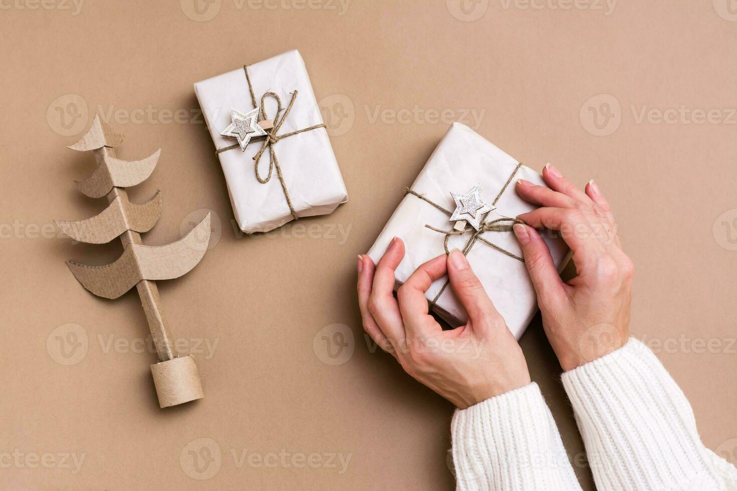 aux femmes mains attacher une arc sur une cadeau dans artisanat papier ai une Noël arbre fabriqué de papier carton sur une beige Contexte. respectueux de la nature décorations pour le vacances. photo