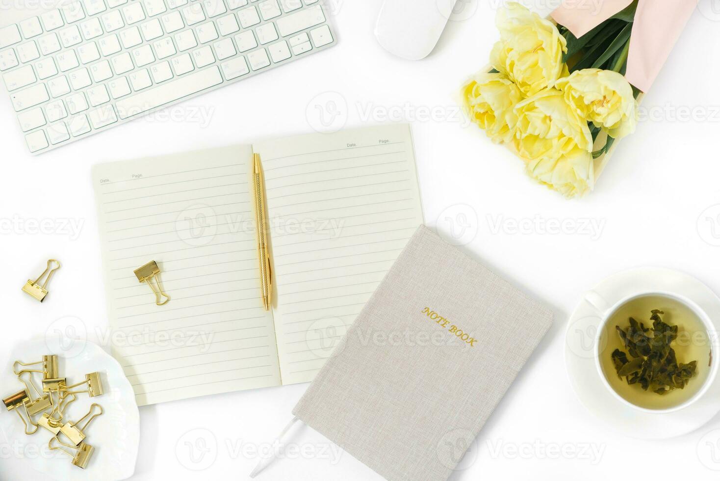 Bureau bureau tableau. plat poser, Haut voir. Accueil Bureau espace de travail de une pigiste ou blogueur. une clavier, une souris, une bouquet de tulipes, une tasse de vert thé, et une bloc-notes avec une stylo. photo