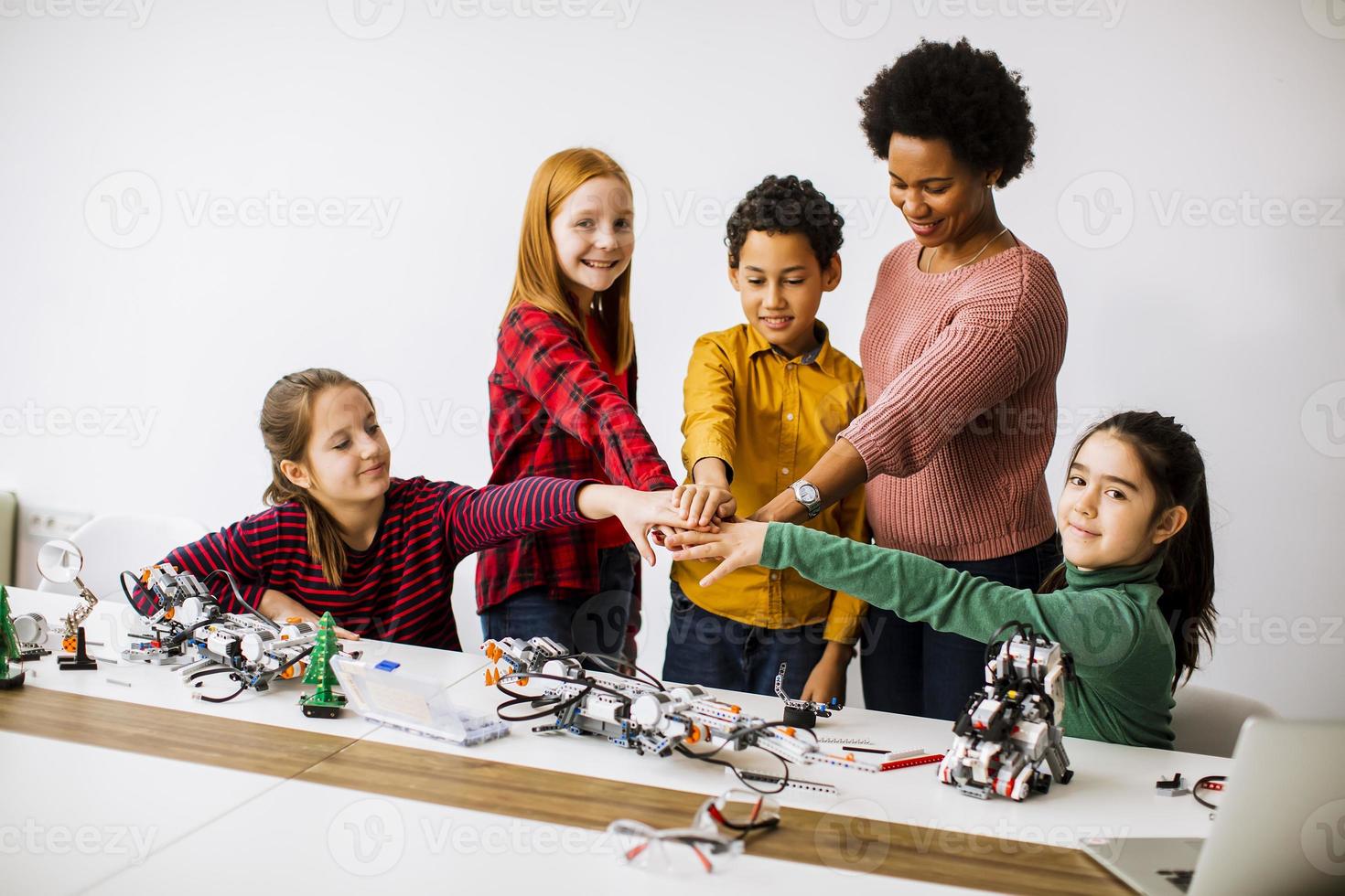 Des enfants heureux avec leur professeur de sciences afro-américaine programmant des jouets électriques et des robots en classe de robotique photo