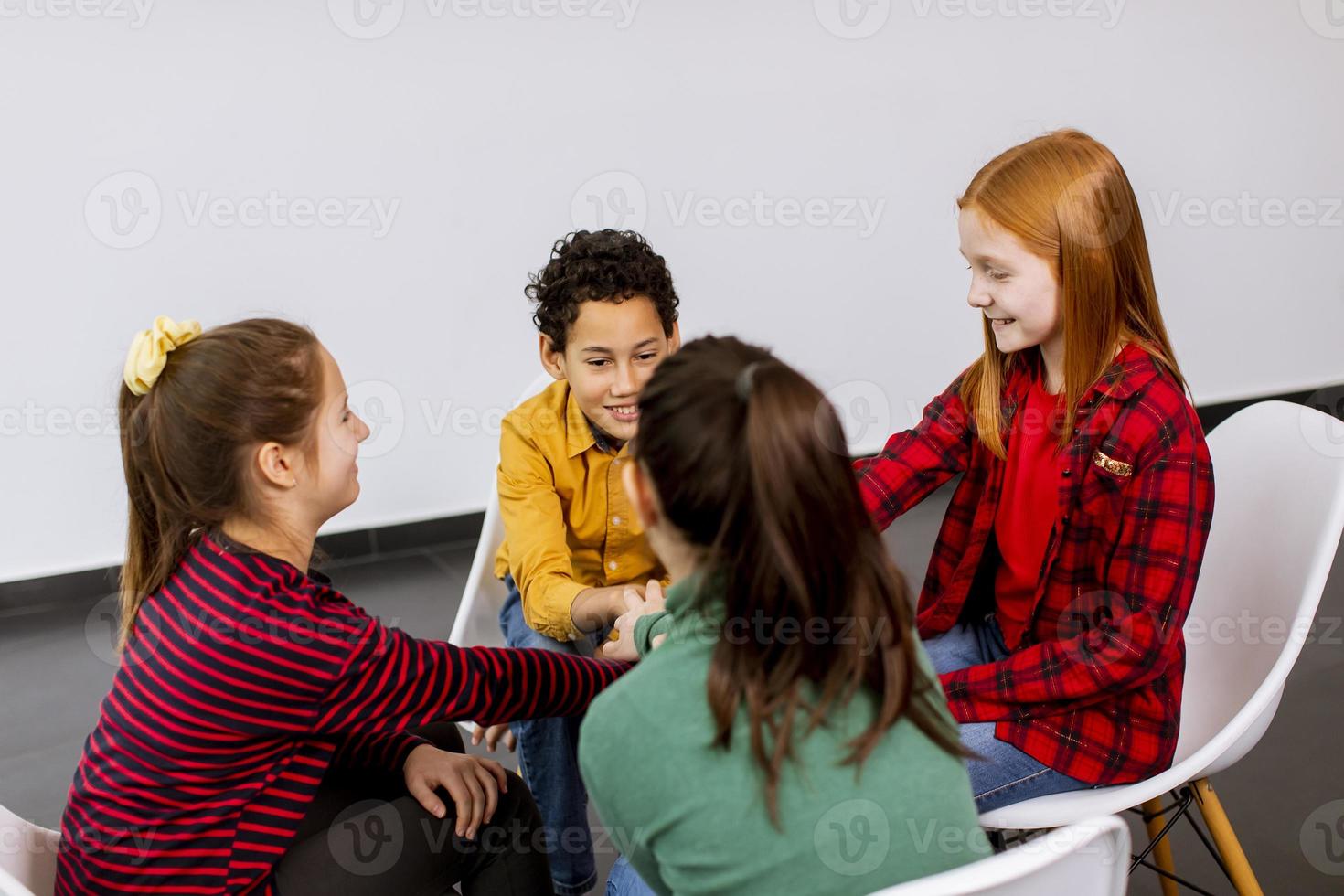 Portrait de mignons petits enfants en jeans parler et assis sur des chaises contre le mur blanc photo