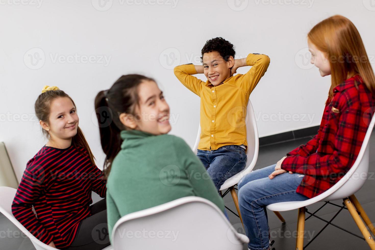 Portrait de mignons petits enfants en jeans parler et assis sur des chaises contre le mur blanc photo