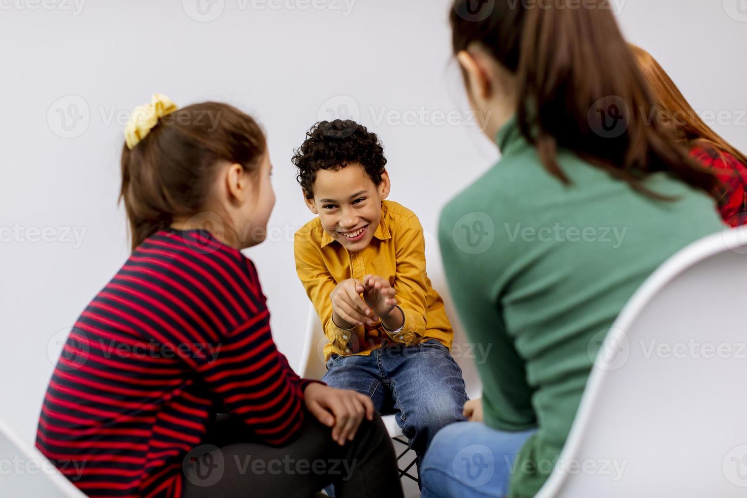 Portrait de mignons petits enfants en jeans parler et assis sur des chaises contre le mur blanc photo