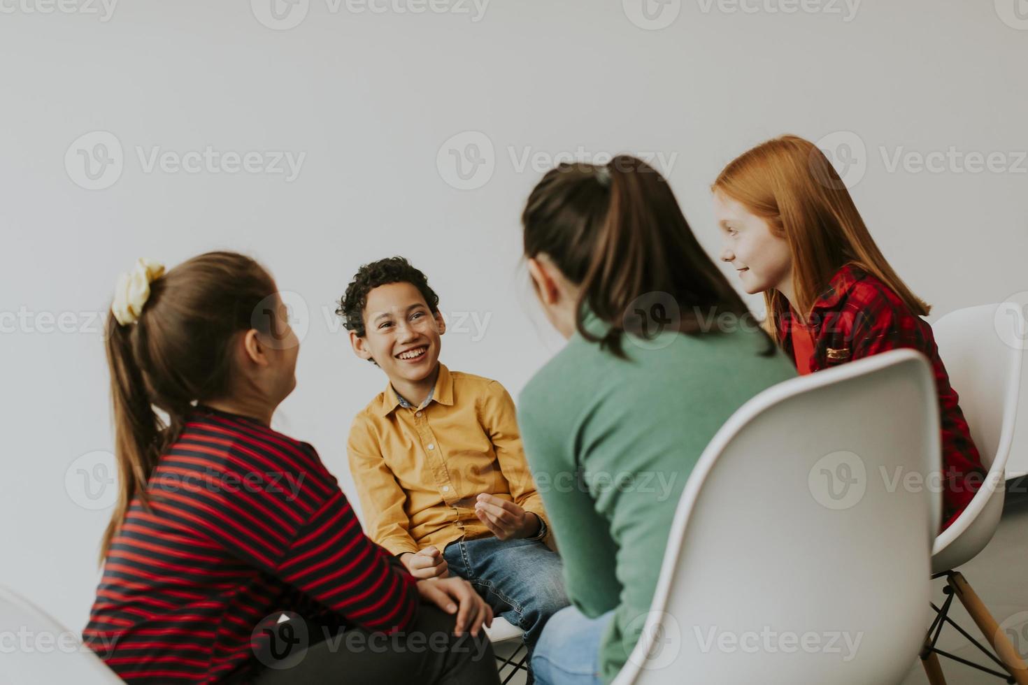 Portrait de mignons petits enfants en jeans parler et assis sur des chaises contre le mur blanc photo