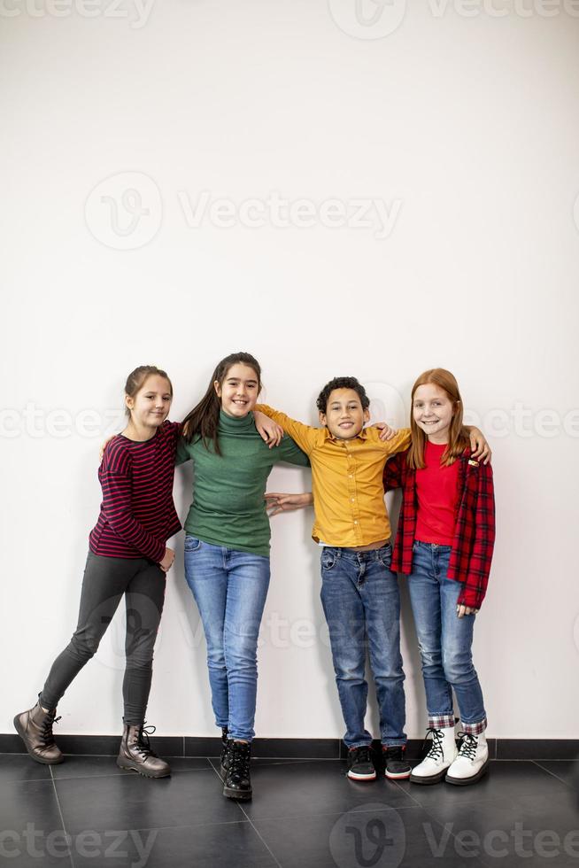 Portrait de mignons petits enfants en jeans regardant la caméra et souriant debout contre le mur blanc photo