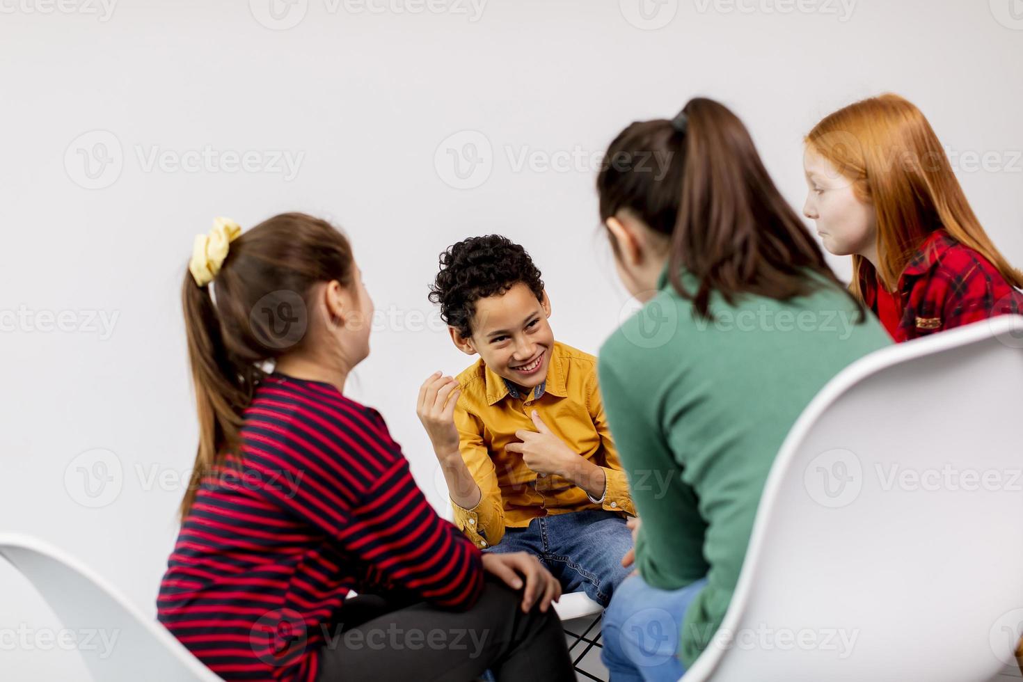 Portrait de mignons petits enfants en jeans parler et assis sur des chaises contre le mur blanc photo