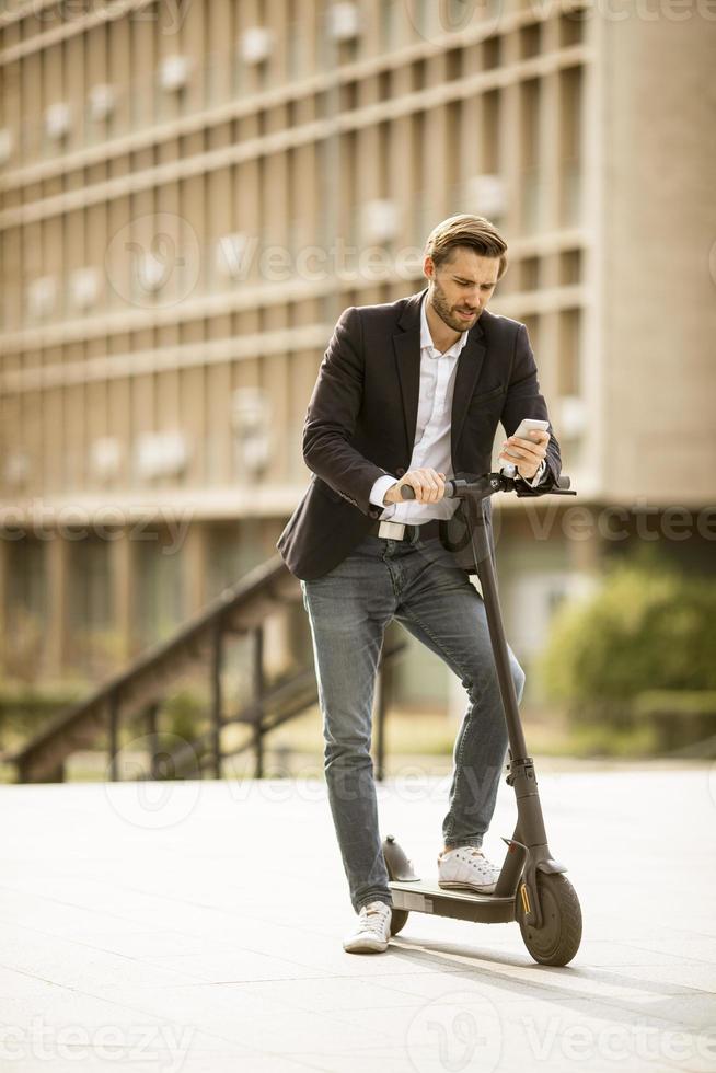 jeune homme d'affaires à l'aide de téléphone mobile sur scooter électrique photo