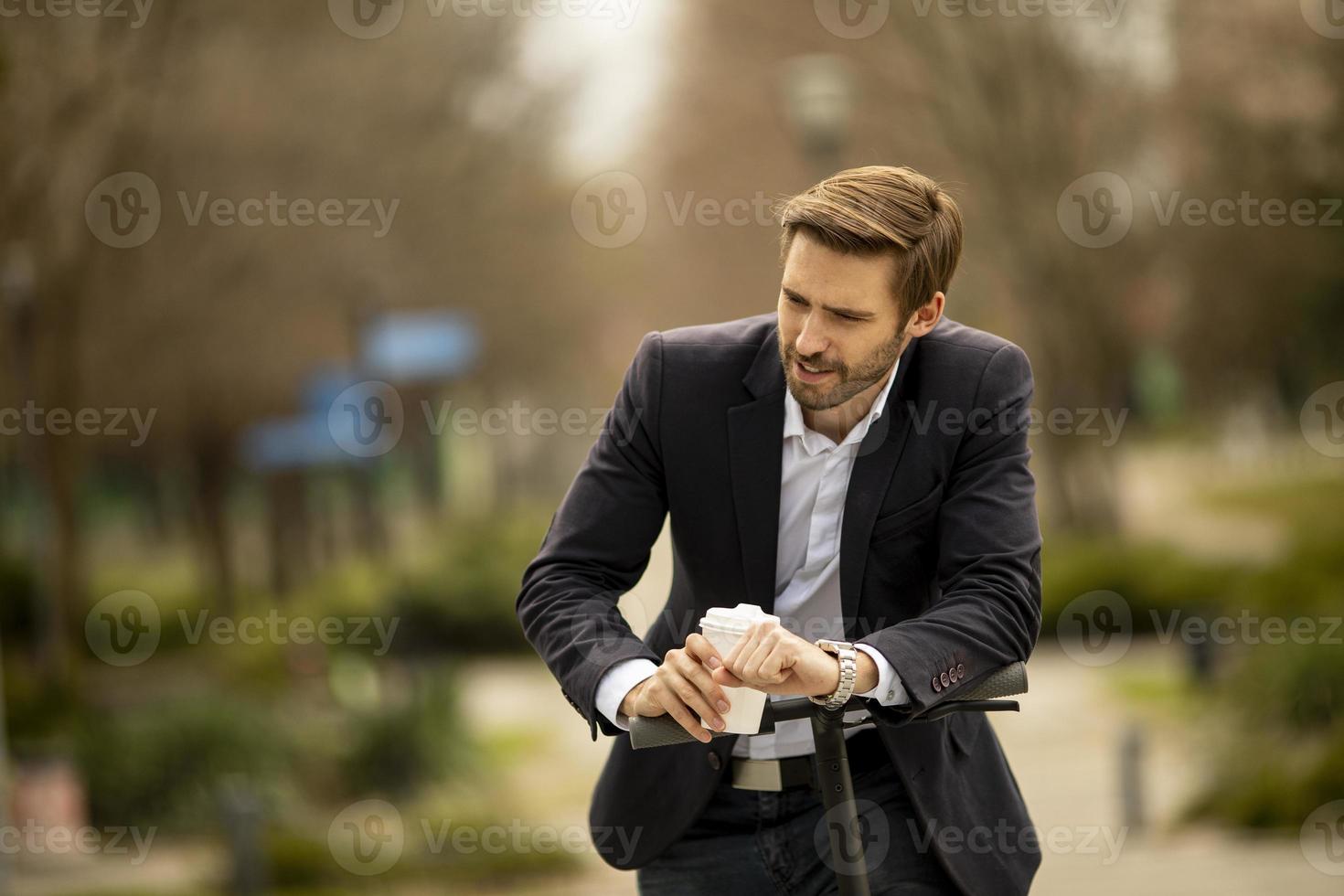 Jeune homme d'affaires buvant une tasse de café à emporter sur un scooter électrique photo