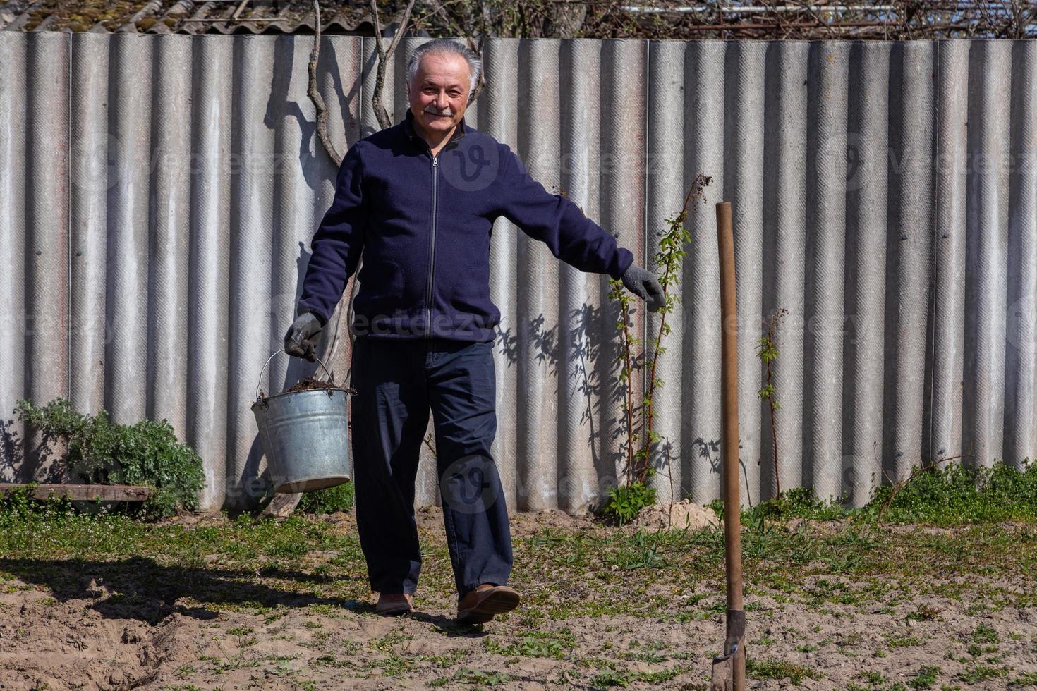 agriculteur adulte avec un seau porte des pommes de terre dans le jardin photo