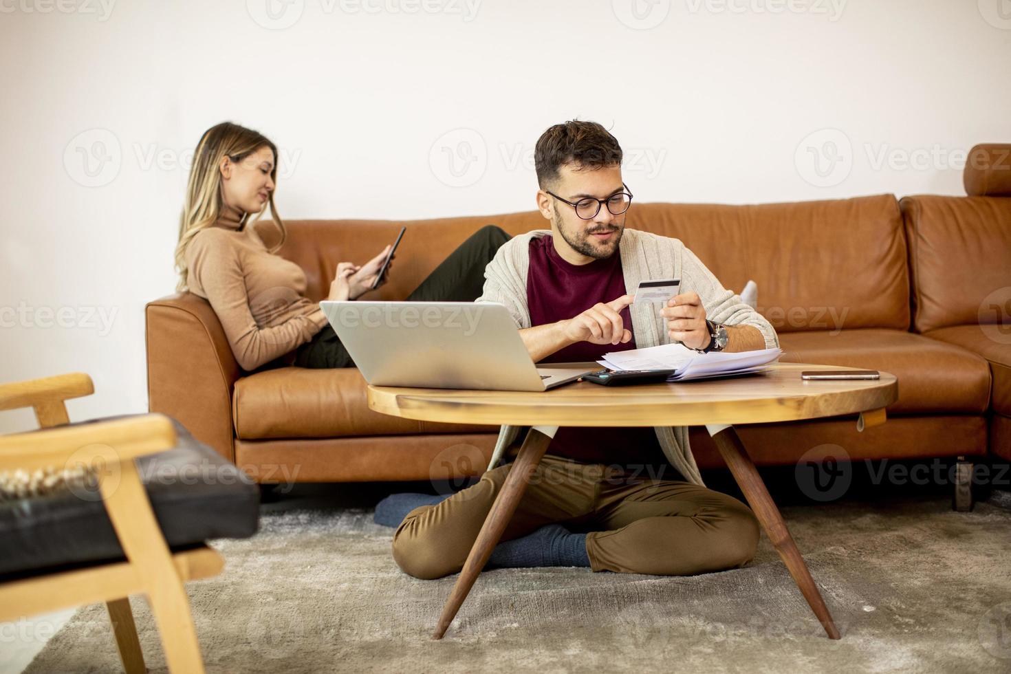 Jeune femme et jeune homme utilisant un ordinateur portable pour le paiement en ligne alors qu'il était assis par canapé à la maison photo