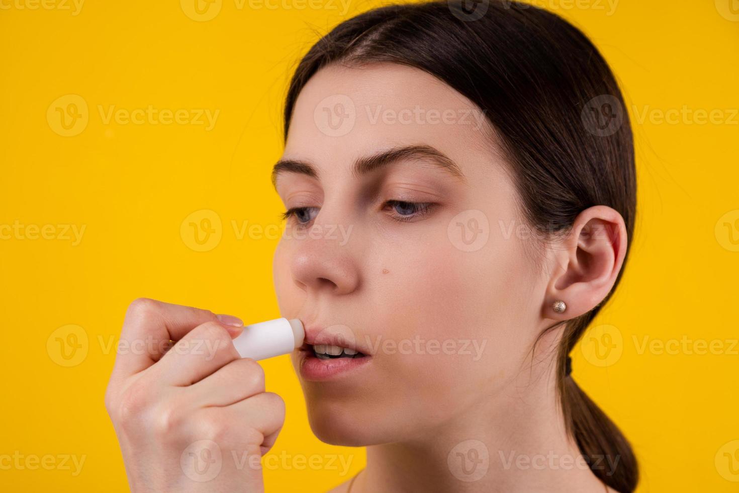 Jolie jeune femme à l'aide de rouge à lèvres hygiénique sur fond jaune photo