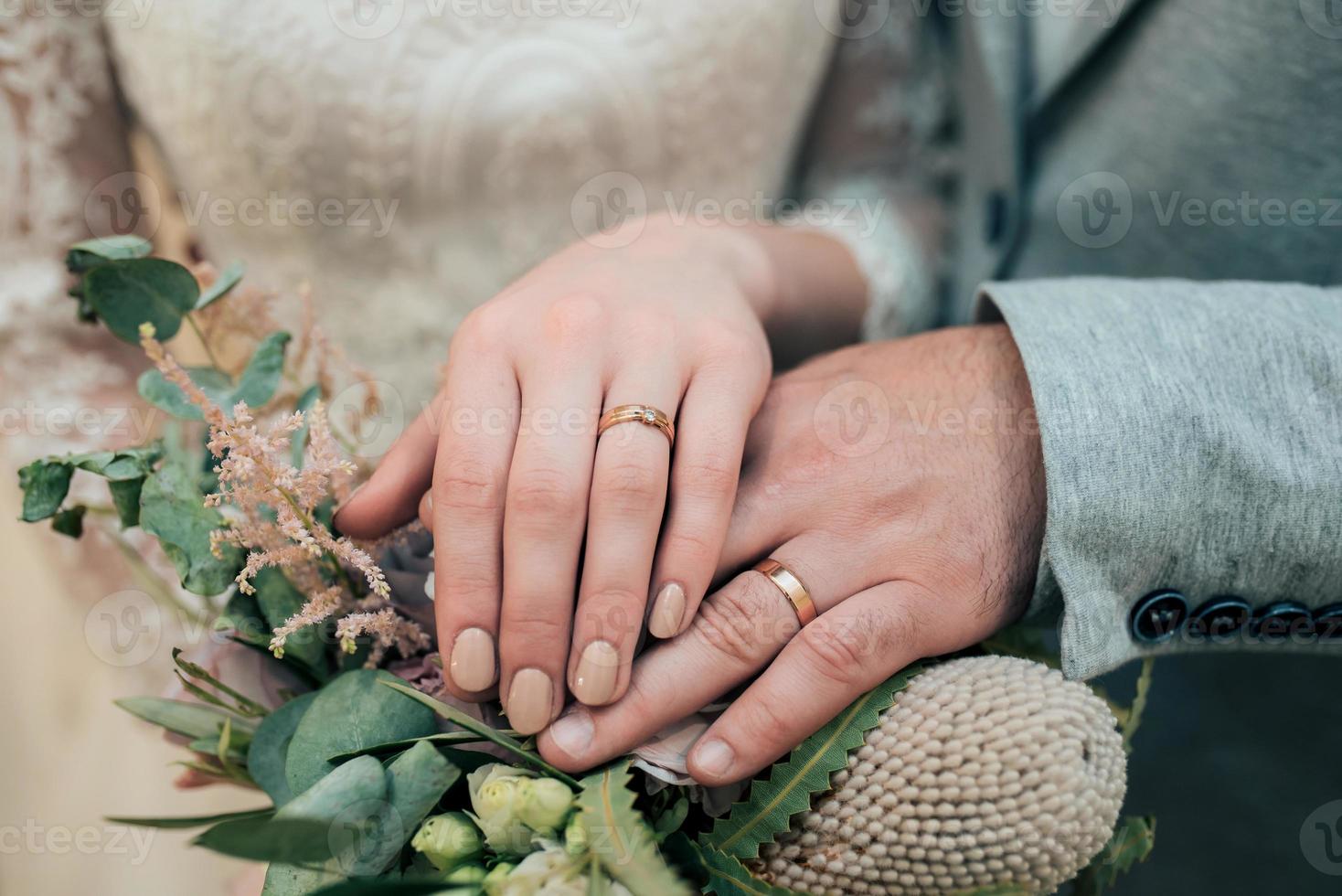 Les mains avec des anneaux de la mariée et le marié sont allongés sur le gros plan du bouquet photo