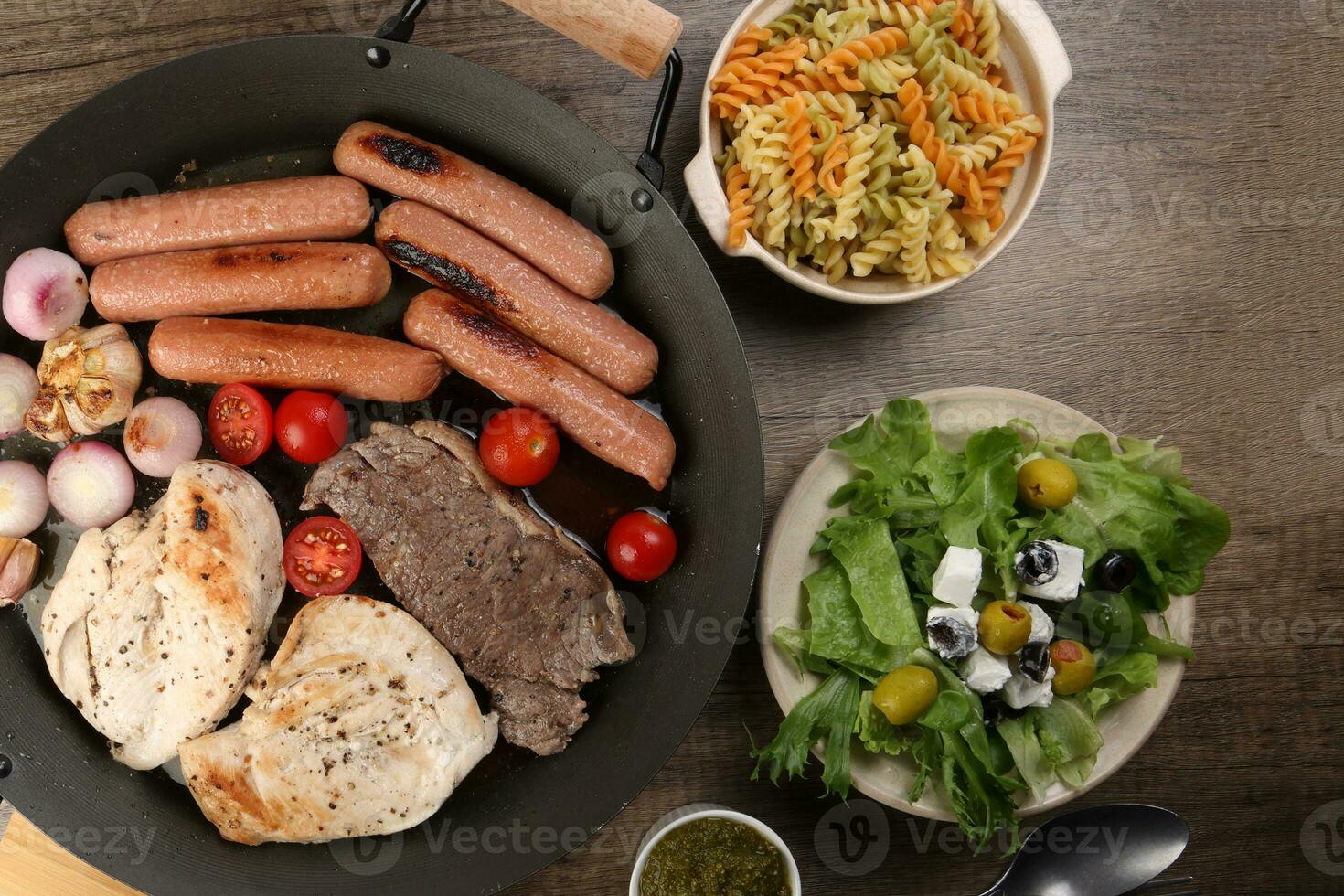 mélanger rencontrer poulet du boeuf steak saucisse tomate oignon Ail frire gril pétrole métal frire la poêle coloré Pâtes vert salade avec fromage olive menthe basilic Pesto sauce planche couteau fourchette cuillère rustique en bois table photo