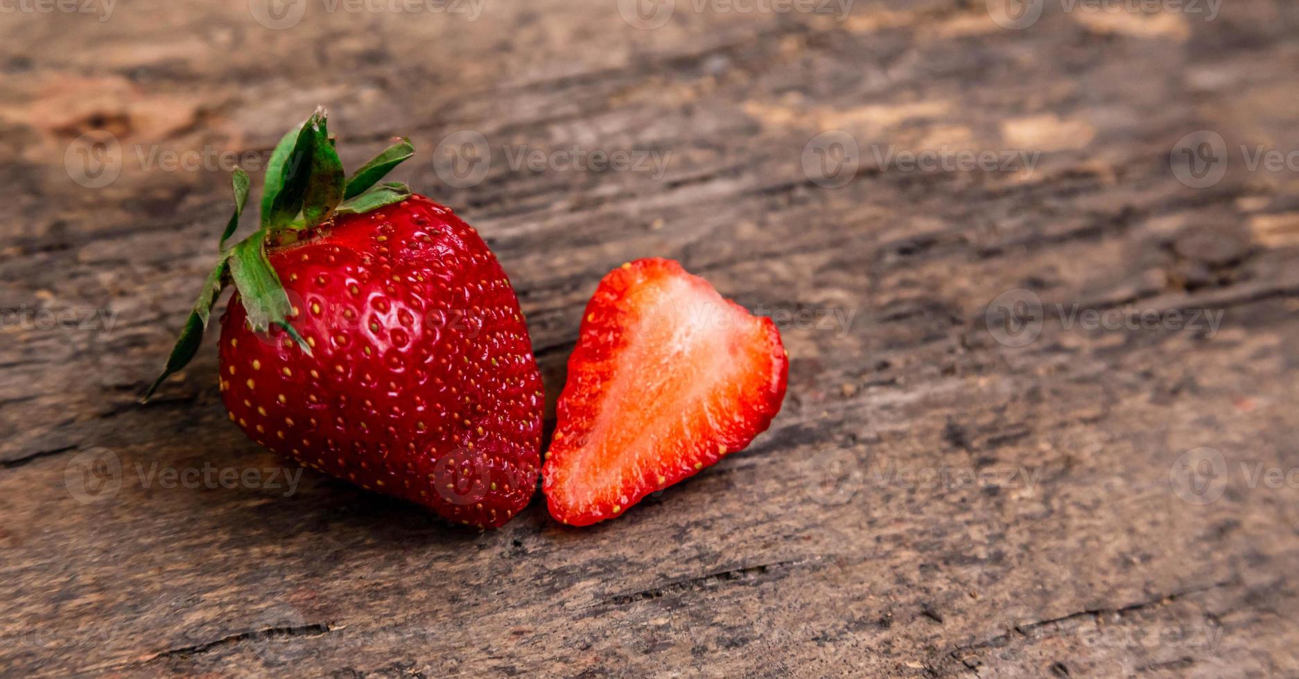 une fraise entière et une demi-fraise sur une surface en bois sombre photo