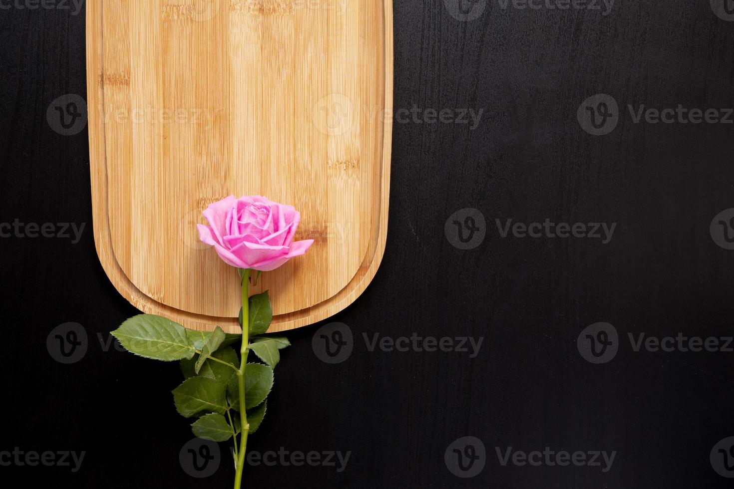 Une rose rose pose sur une planche à découper en bois sur un fond sombre photo