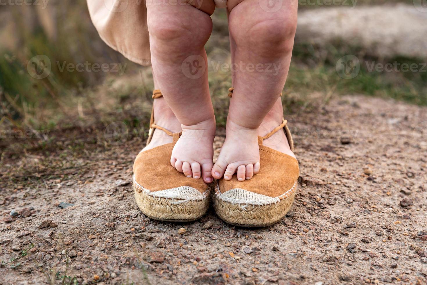 les jambes d'un bébé se tiennent sur les pieds de la mère photo