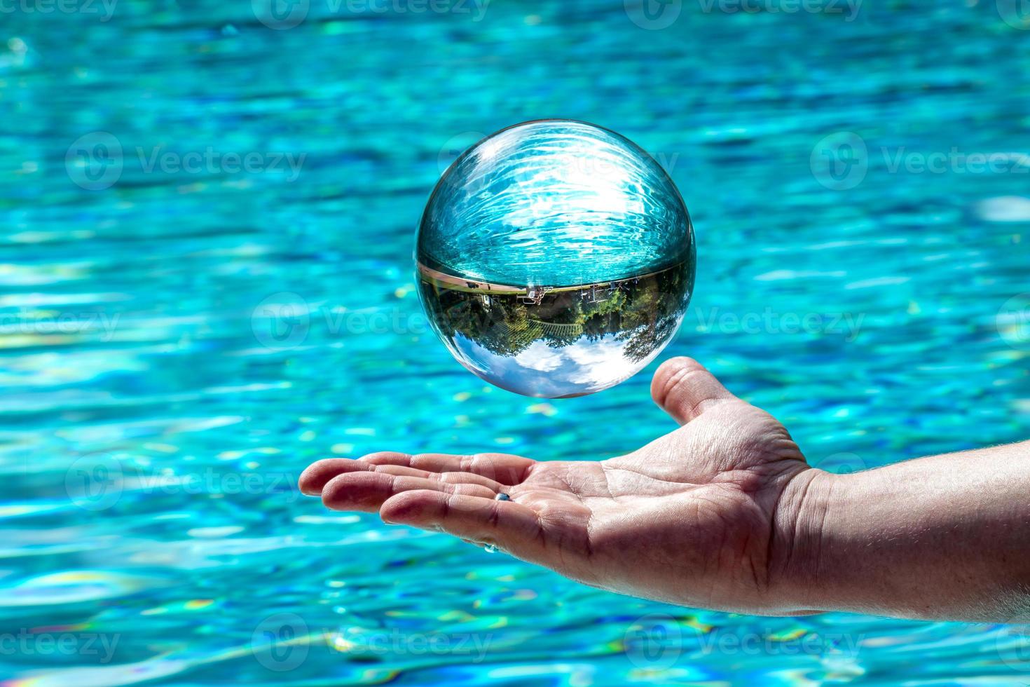 Boule de verre plane au-dessus d'une main en face de fond de l'eau avec ciel et arbres en miroir photo