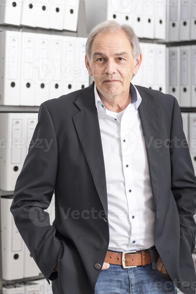 Homme d'âge moyen avec chemise blanche est debout devant un mur d'étagère avec des documents photo