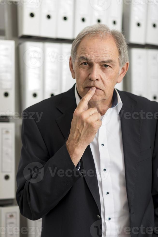 Homme d'âge moyen avec chemise blanche est debout devant un mur d'étagère avec des documents photo