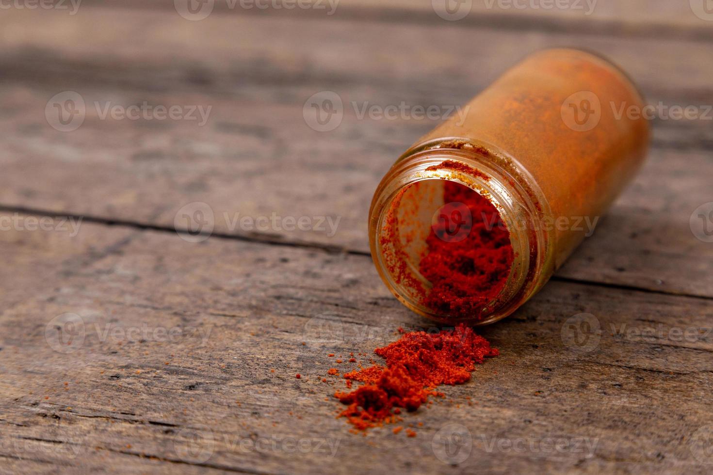Piment épices en poudre colorées dispersées à partir de la bouteille sur fond de bois photo