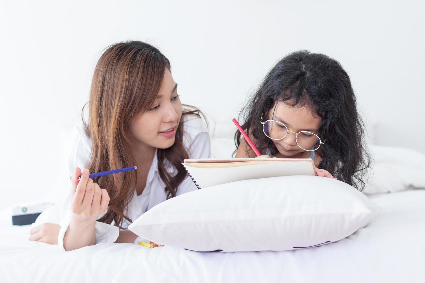 mère asiatique enseigne ses devoirs à sa fille à la maison en vacances photo