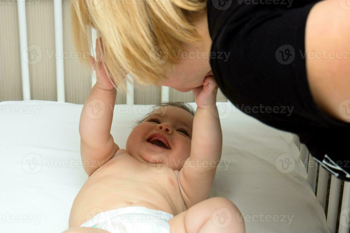 joyeux bébé s'étire le sien bras à le sien mère penché plus de le lit de bébé photo