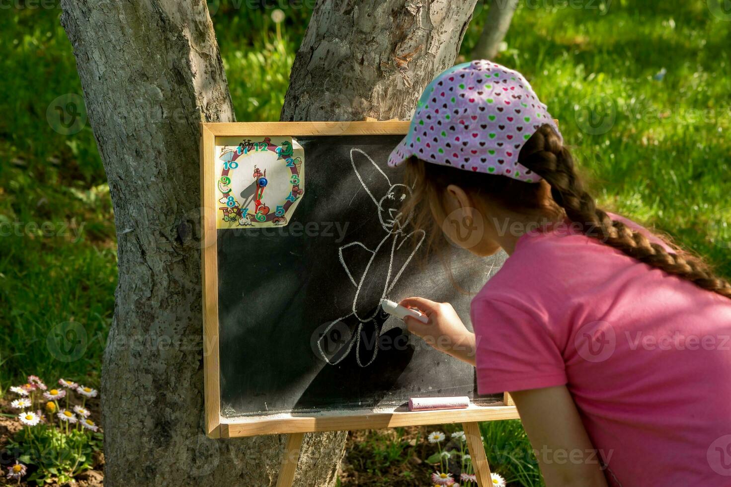 une fille dans une casquette dessine sur une ardoise conseil, sur une été ensoleillé journée dans le jardin photo