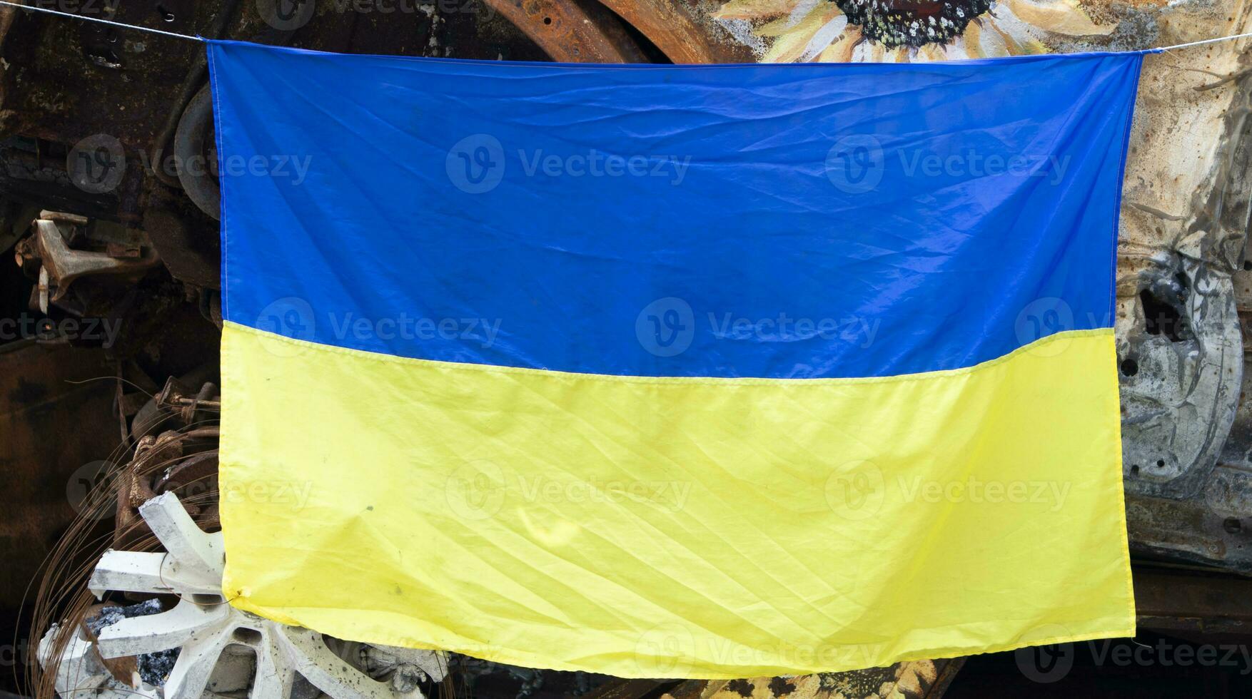 le nationale drapeau de Ukraine contre le Contexte de ruines et rouillé métal de détruit voitures. guerre dans Ukraine. une bleu jaune drapeau agitant dans le vent en dessous de le Soleil dans une bombardé ville. photo