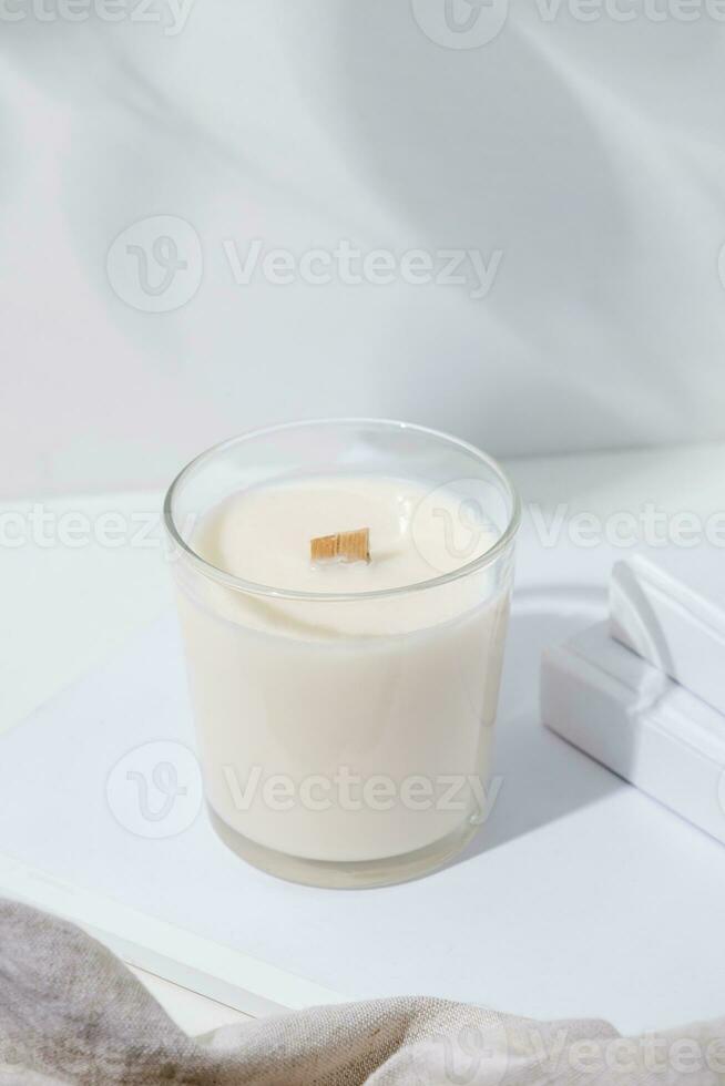 blanc arôme bougie dans verre pot avec en bois mèche sur blanc Contexte avec livres et tissu photo