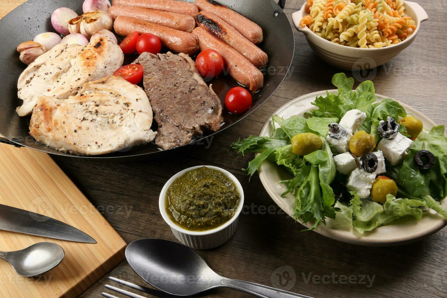 mélanger rencontrer poulet du boeuf steak saucisse tomate oignon Ail frire gril pétrole métal frire la poêle coloré Pâtes vert salade avec fromage olive menthe basilic Pesto sauce planche couteau fourchette cuillère rustique en bois table photo