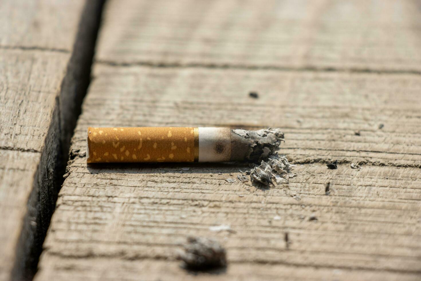 brûlant cigarette proche en haut sur une cassé en bois surface. cigarette sur une en bois surface proche en haut. mauvais pour la santé fumeur habitude et cigare dépendance. nicotine dépendance concept avec une brûlé cigarette et cendres. photo