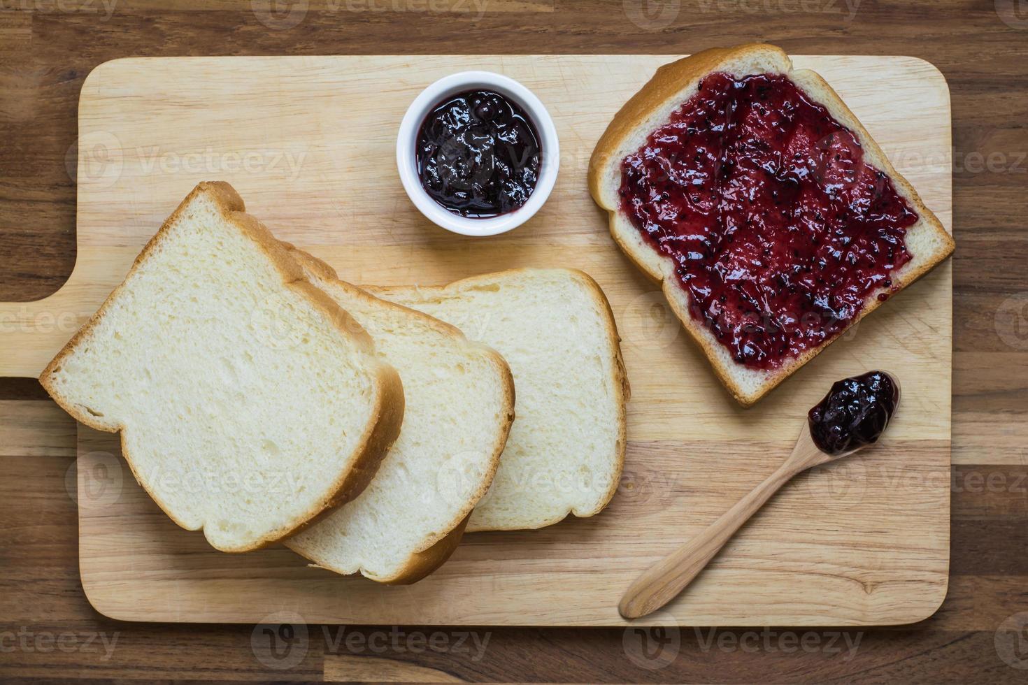 Vue de dessus des tranches de pain maison avec de la confiture de cassis sur la planche de bois photo