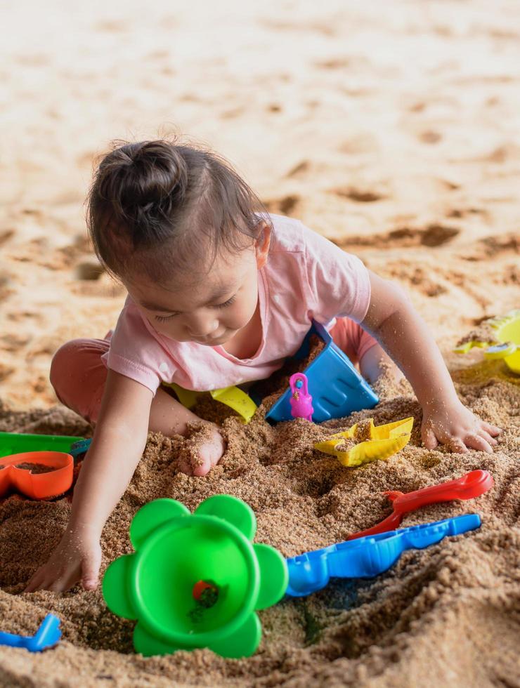 Jolie petite fille asiatique jouant avec des jouets de plage sur la plage photo