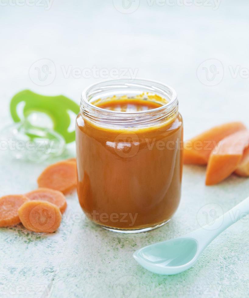 Bébé carotte en purée avec cuillère dans un bocal en verre photo