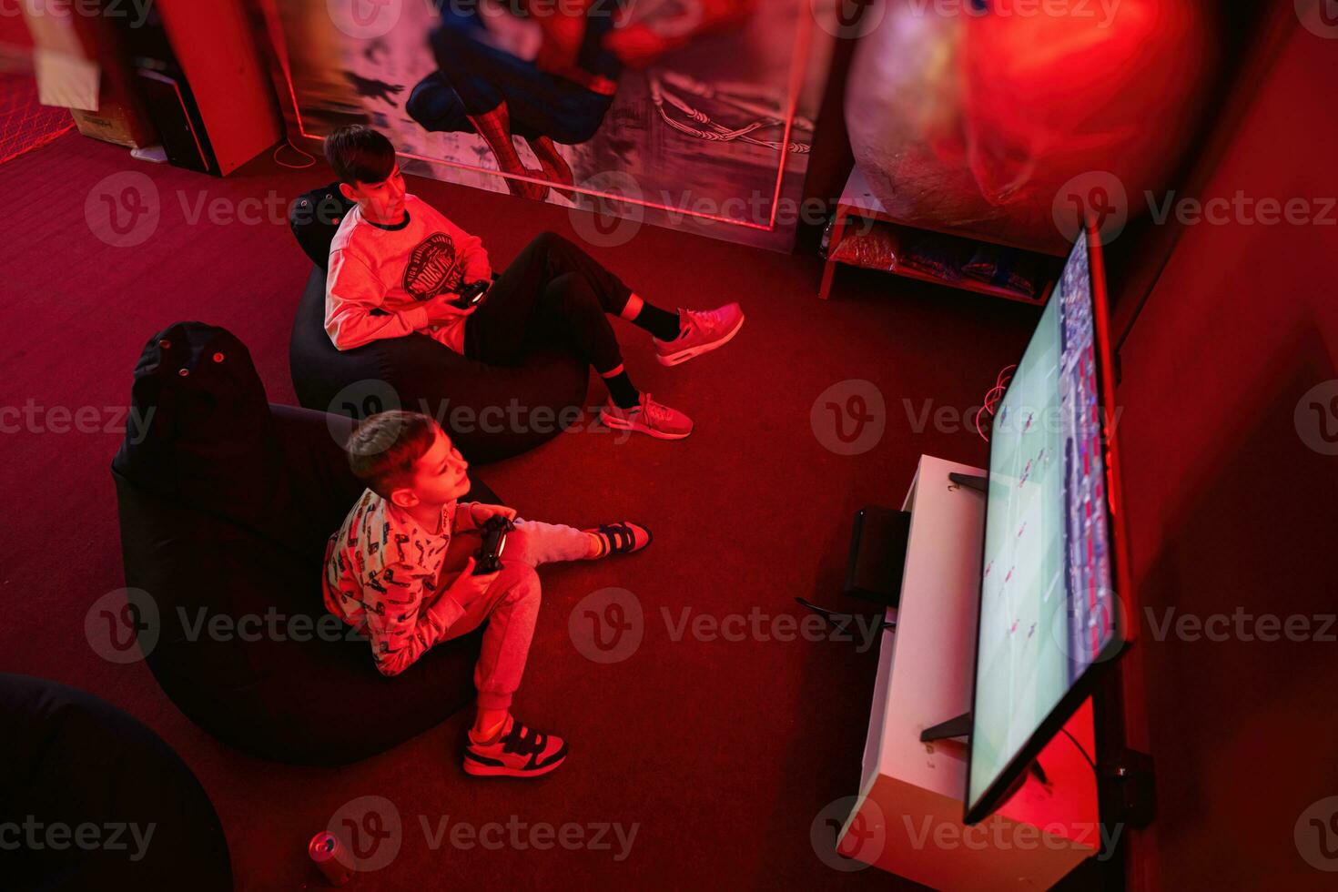 deux garçons les joueurs jouer Football manette de jeu vidéo Jeu console dans rouge jeu chambre. photo