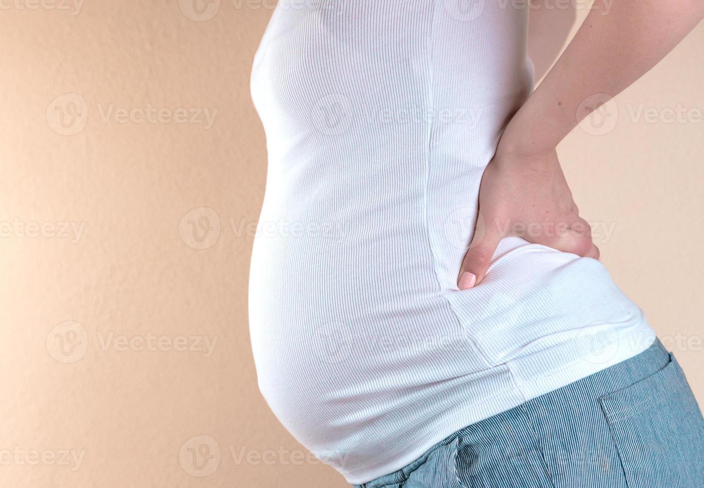 Image recadrée de belle femme enceinte touchant son ventre et gardant une main sur son dos photo