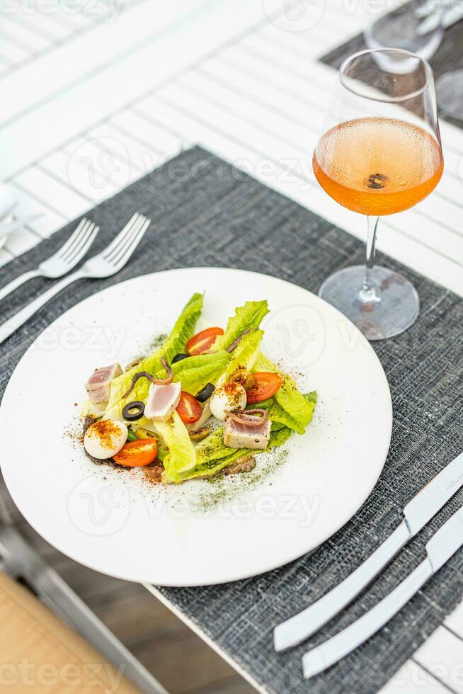 délicieux gros légumes verts salade avec Rose du vin. luxe restaurant, blanc en bois table et élégant coutellerie et table installation. fermer plat, gourmet nourriture concept photo